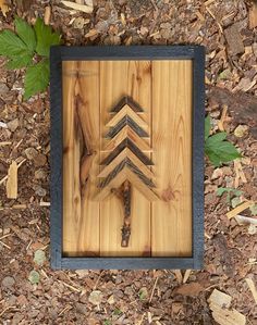 a wooden plaque with an arrow on it sitting in the ground next to some leaves