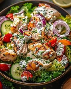 a salad with chicken, cucumber, tomatoes and onions in a bowl on a table