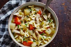 a bowl of chicken noodle soup on top of a checkered cloth with a spoon