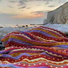 there is a crocheted blanket laying on the rocks by the water at sunset