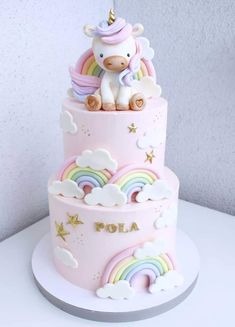 a pink cake with a unicorn on top and rainbows in the clouds around it