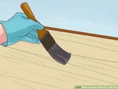 a person in blue gloves holding a paintbrush on top of a wooden floor next to a wall