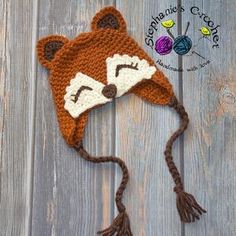 a crocheted hat with a fox face on it sitting on a wooden surface