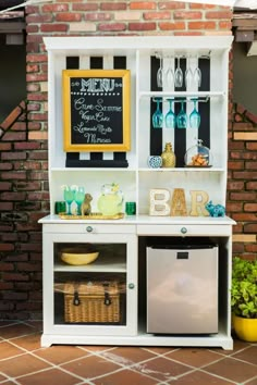 a white shelf with wine glasses and bottles on it, next to a brick wall