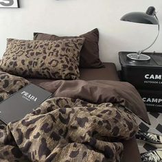 an unmade bed with leopard print comforter and pillows on the floor next to a lamp