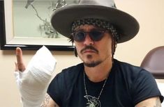 a man wearing a hat and sunglasses holds up a bandaged hand