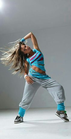 a woman is dancing with her hair in the air while wearing sweatpants and sneakers