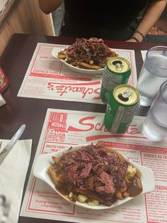 two plates of food are sitting on the table with sodas and water in front of them