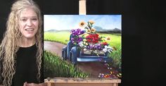 a woman standing next to an easel with flowers in the back and a painting on it