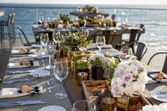 a long table set up with flowers and candles for an outdoor dinner by the ocean