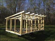 a wooden structure sitting in the middle of a grass covered field with trees behind it