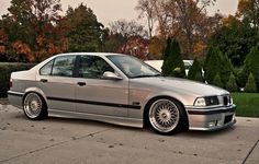 a silver car parked on the side of a road next to some bushes and trees