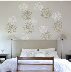 a bed with white sheets and pillows in front of a wall decorated with flower stencils