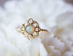 an opalite and diamond ring sits on top of a white peonie flower