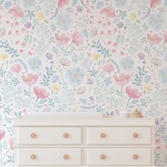 a white dresser sitting next to a wall with flowers on it