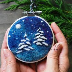 a hand holding a blue and white felt ornament with trees in the snow