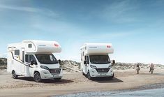 two white motorhomes parked on the beach next to each other