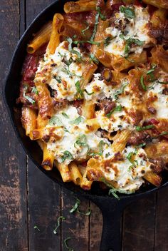 a skillet filled with pasta and cheese on top of a wooden table next to a fork