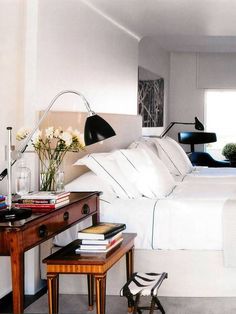 a white bed sitting next to a wooden table with flowers on it in a bedroom