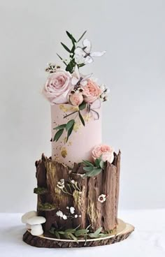 a three tiered cake decorated with flowers and leaves on a tree stump, against a white background