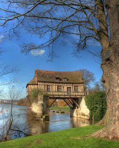 an old bridge over a body of water with a house in the background and trees around it