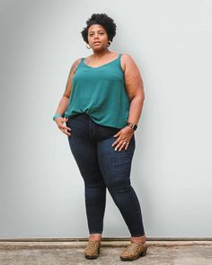 a woman standing in front of a white wall with her hands on her hips and looking at the camera