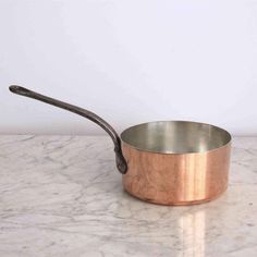 an empty copper pan on a marble countertop with a metal spoon sticking out of it