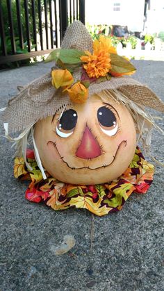 a pumpkin with a scarecrow's hat and leaves on it sitting on the ground