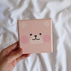 a hand holding up a pink square with a bear face painted on it