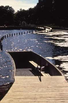 a person sitting on a bench next to the water at a pier in front of some trees