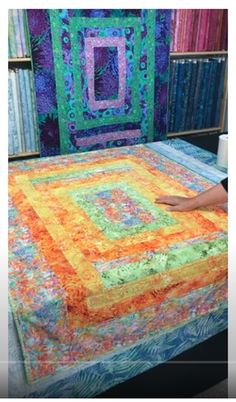 a bed with a colorful quilt on it in a room full of bookshelves