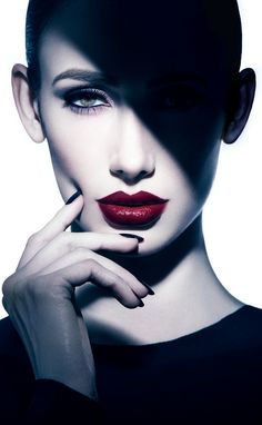 a woman with dark makeup and red lipstick posing for the camera, her hand on her chin