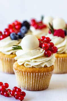 two cupcakes with white frosting and berries on top, sitting next to each other