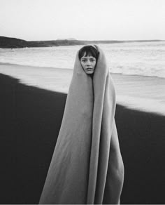 a woman wrapped in a blanket on the beach with her head peeking out from behind