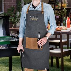 a man wearing an apron and holding a beer standing in front of a bbq