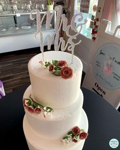 a three tiered cake with flowers on the top is sitting on a black table