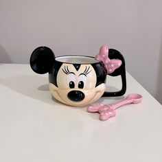 a mickey mouse mug with a pink spoon next to it on a white countertop