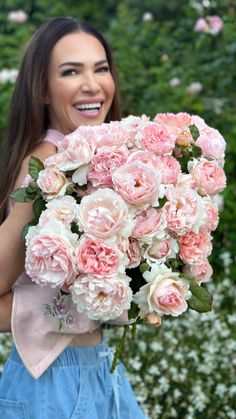 a woman holding a bouquet of pink flowers in front of her face and smiling at the camera