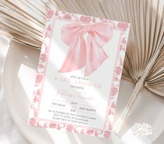 a pink and white baby shower is on a plate next to an open fan,