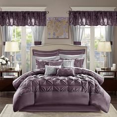 a bed in a bedroom with purple comforter and pillows