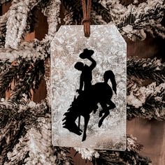 a christmas ornament with a cowboy on a horse hanging from a pine tree