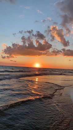 the sun is setting over the ocean with clouds in the sky and waves on the beach