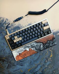 a computer keyboard sitting on top of a blue and white marbled surface next to a black cord