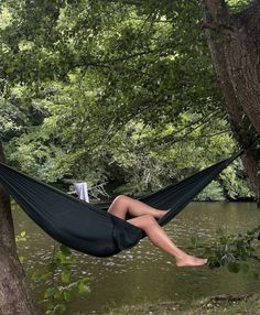 a woman is sitting in a hammock on the river bank with her legs crossed