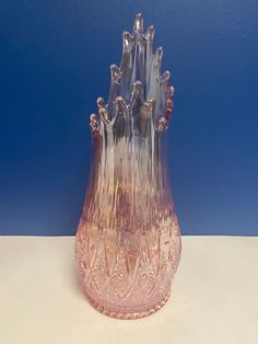 a pink glass vase sitting on top of a white table next to a blue wall