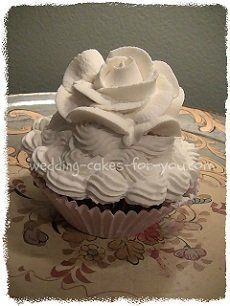 a cupcake with white frosting and a rose on top is sitting on a plate