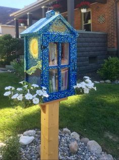 a blue book case sitting on top of a wooden pole next to flowers and rocks