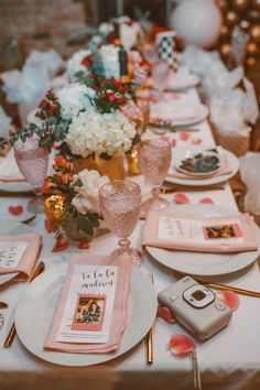 the table is set with pink and white plates, napkins, silverware, and flowers