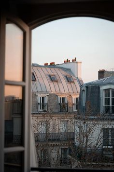 an open window shows the view of buildings and rooftops in paris, france at sunset