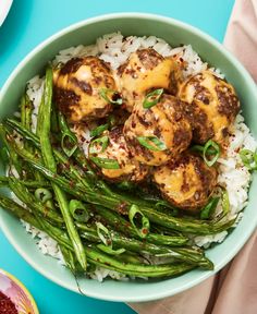 a bowl filled with rice and meat covered in gravy on top of green beans